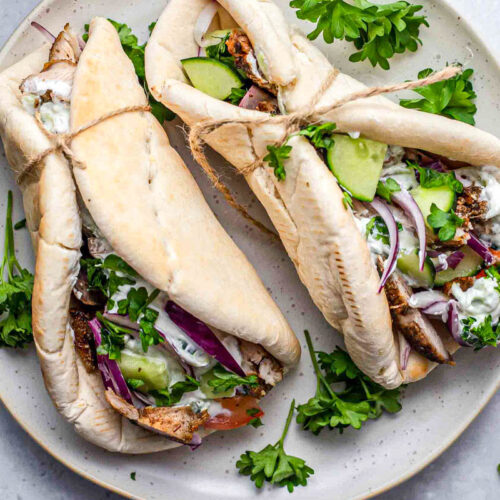 two chicken gyro in pitas on plate with parsley around.