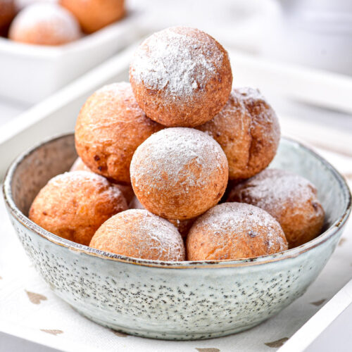 pyramid of round cheese donuts in bowl sitting on white tray.