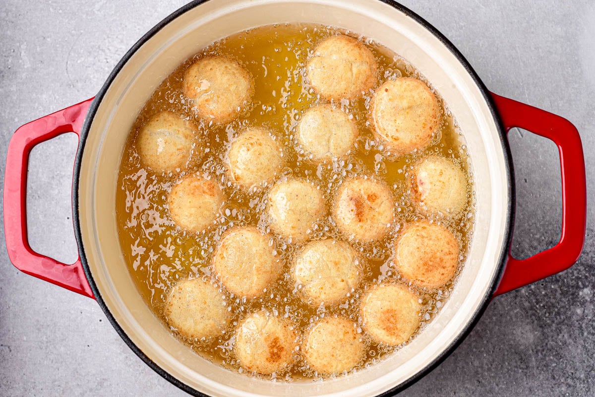 donut holes deep frying in large pot of oil with red handles.