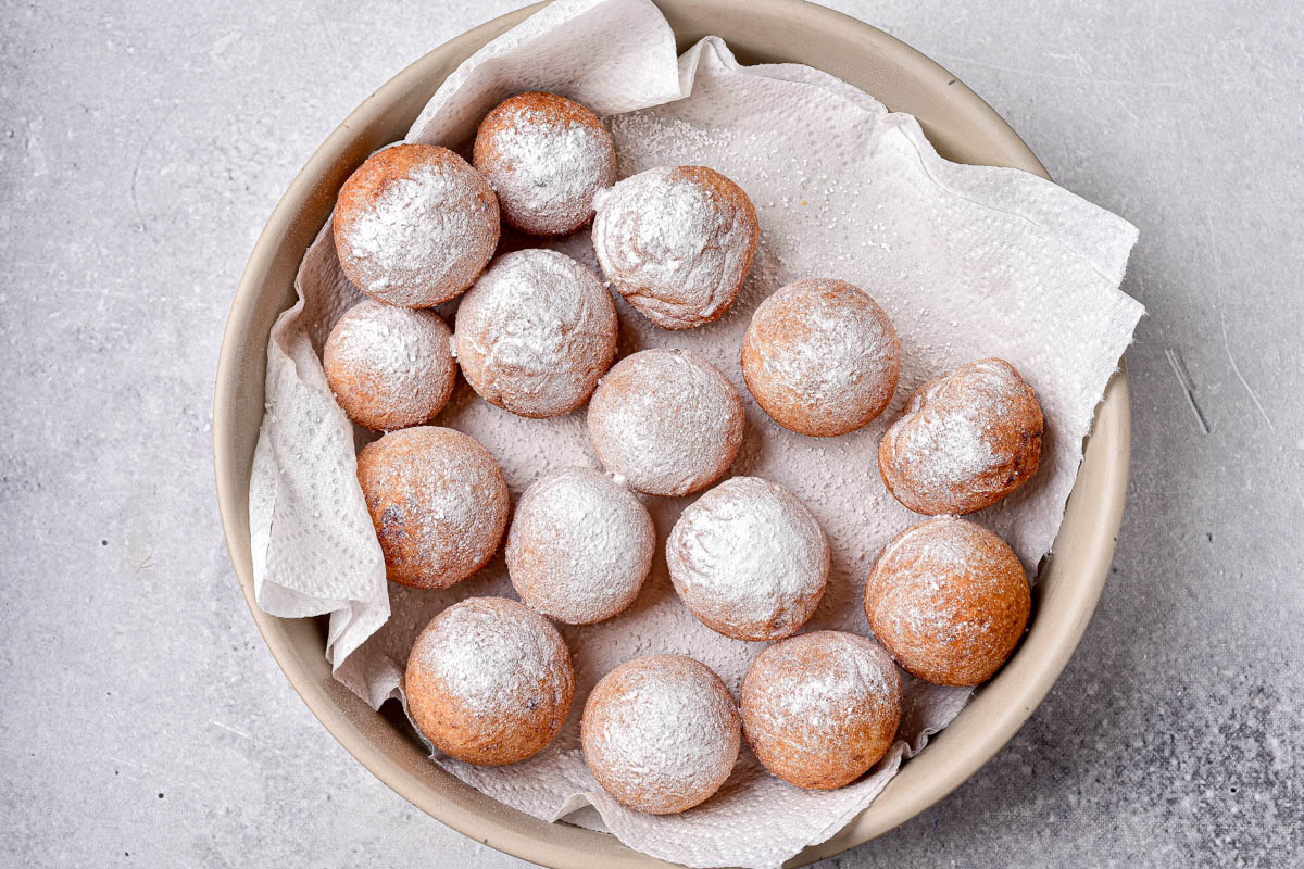 cooked donut holes covered in powdered sugar sitting on plate.