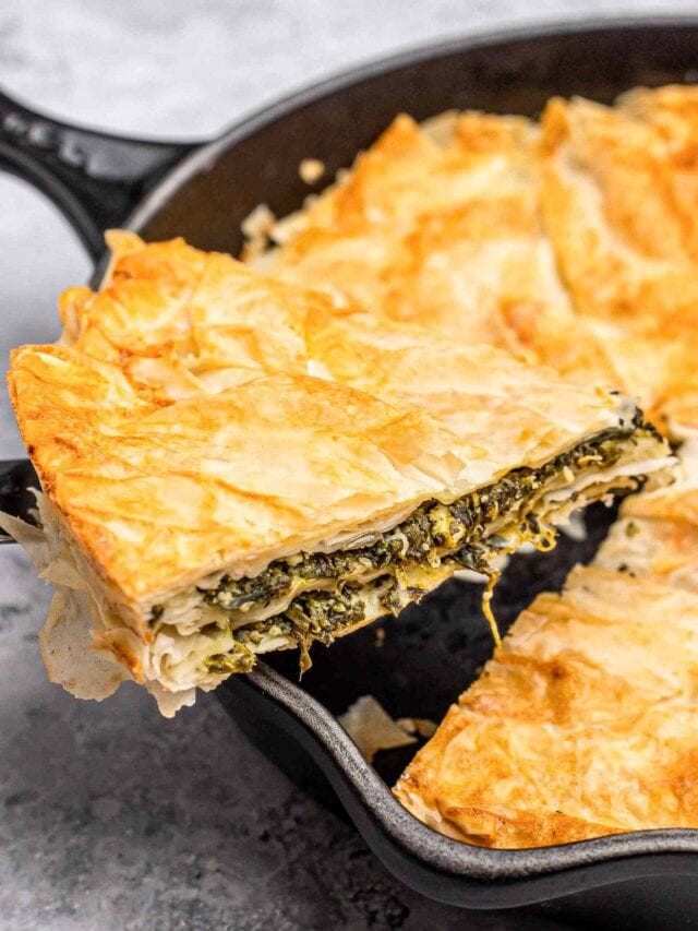 slice of spinach-filled burek being lifted from black cast iron pan.