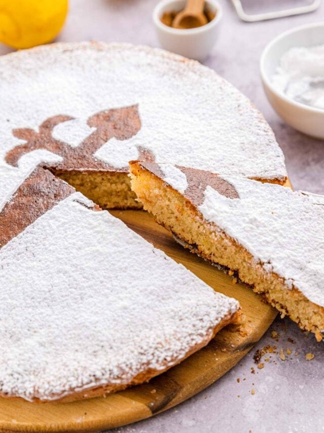 slice of spanish almond cake being removed from larger cake on wooden board.