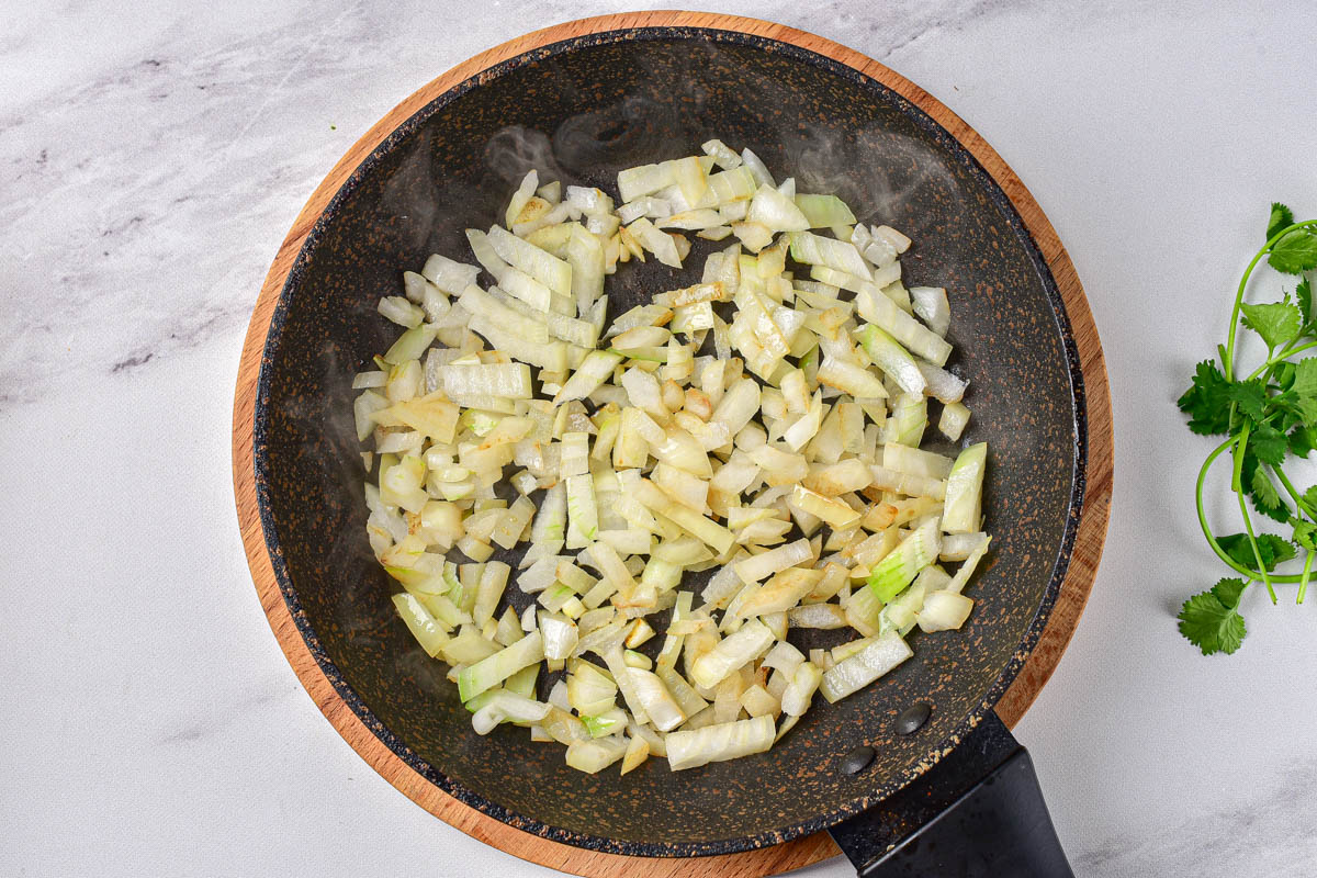 chopped onion frying in black frying pan with white counter around.