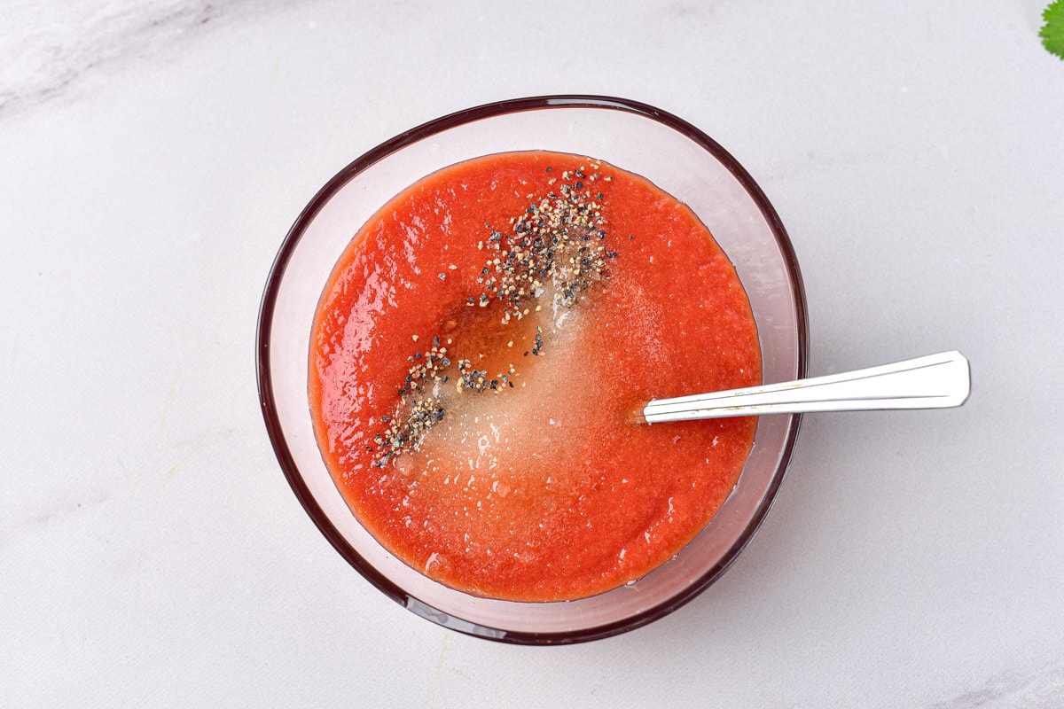 tomato puree with other spices on top in clear glass bowl with silver spoon sticking out.