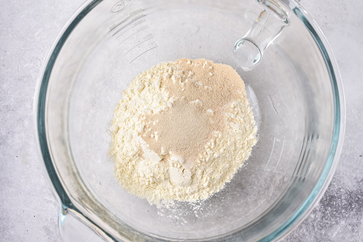 dry yeast and flour in clear glass bowl on marble counter seen from above.