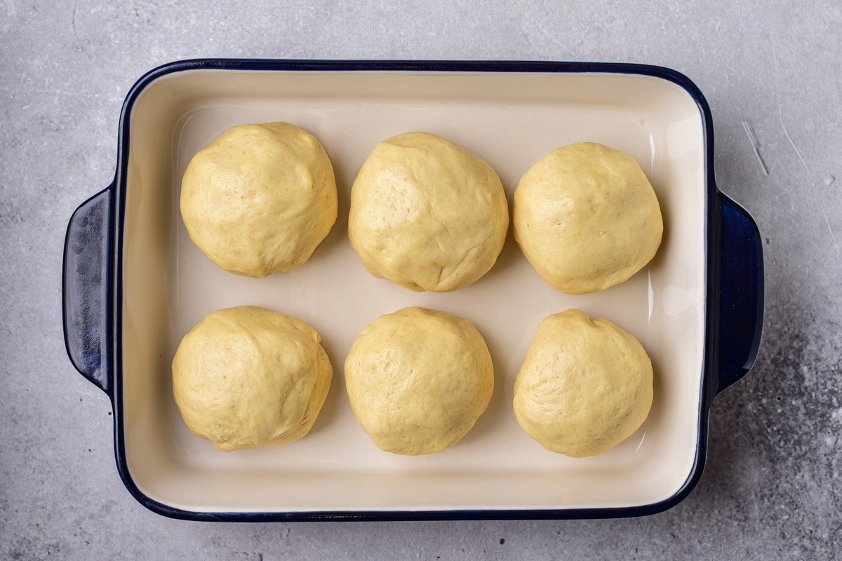 six balls of raw bread dough in large baking dish on counter.