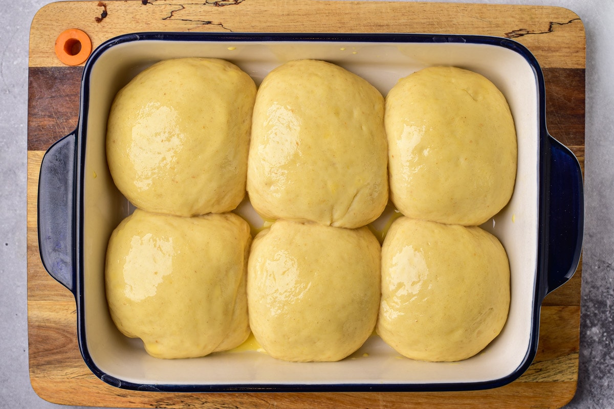 six risen balls of bread roll dough in glass dish on counter.