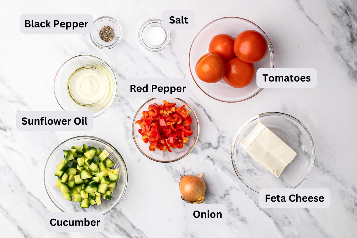 ingredients to make a shopska salad in bowls with labels on marble counter.