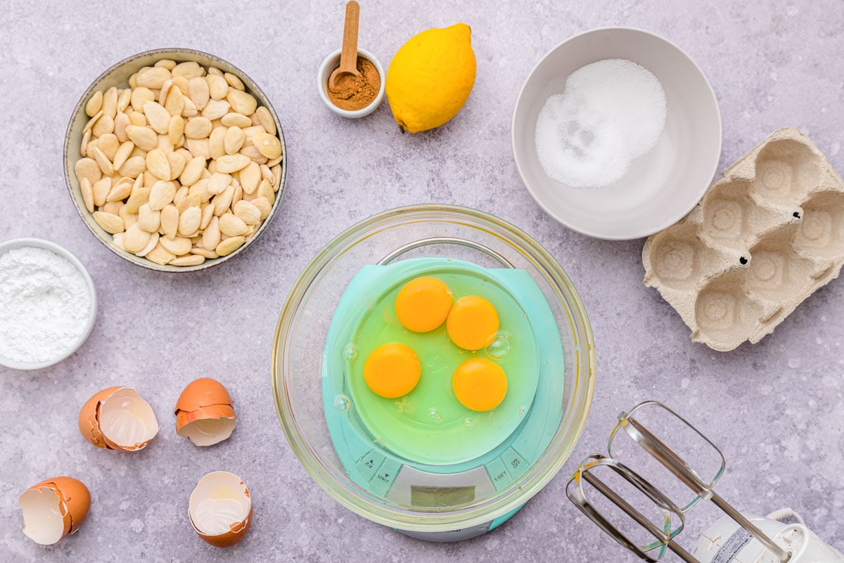 eggs in bowl being weighed with other ingredients around on counter.