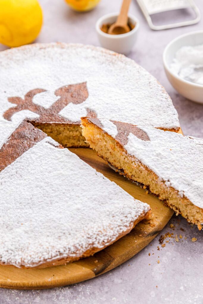 slice of spanish almond cake being removed from larger cake on wooden board.