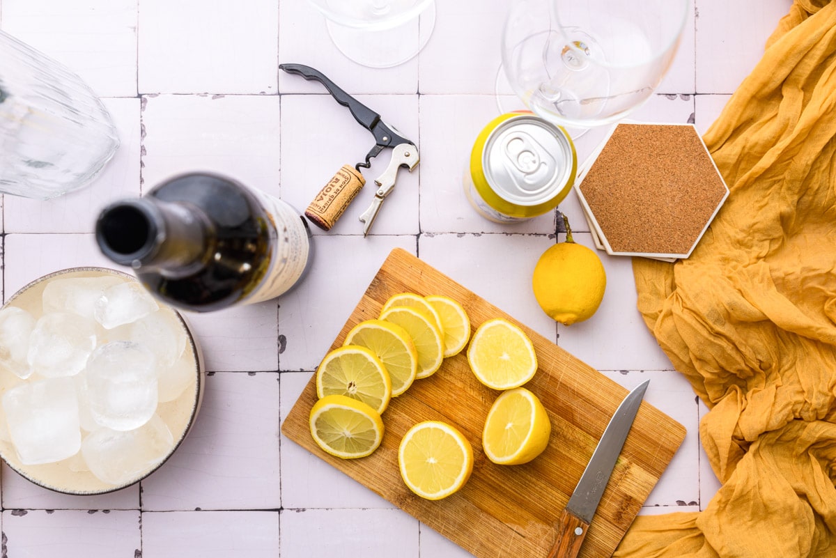 slices of lemon on wooden cutting board with knife and wine bottle beside.