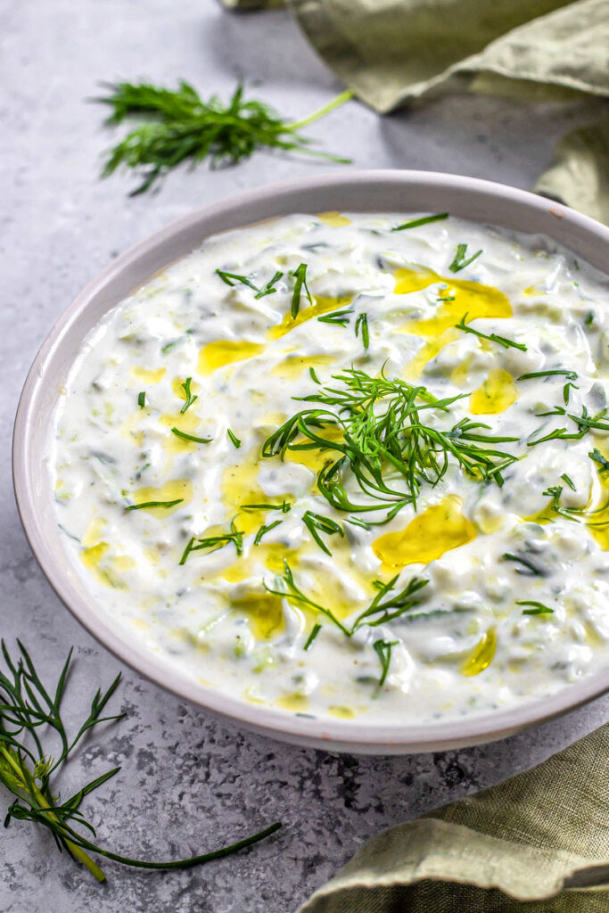 large grey bowl of white tzatziki with fresh dill and oil on top.
