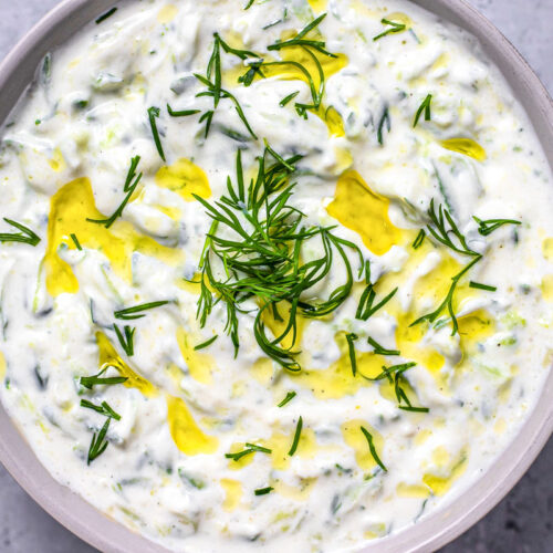 bowl of greek tzatziki with dill and oil on top with grey counter around.
