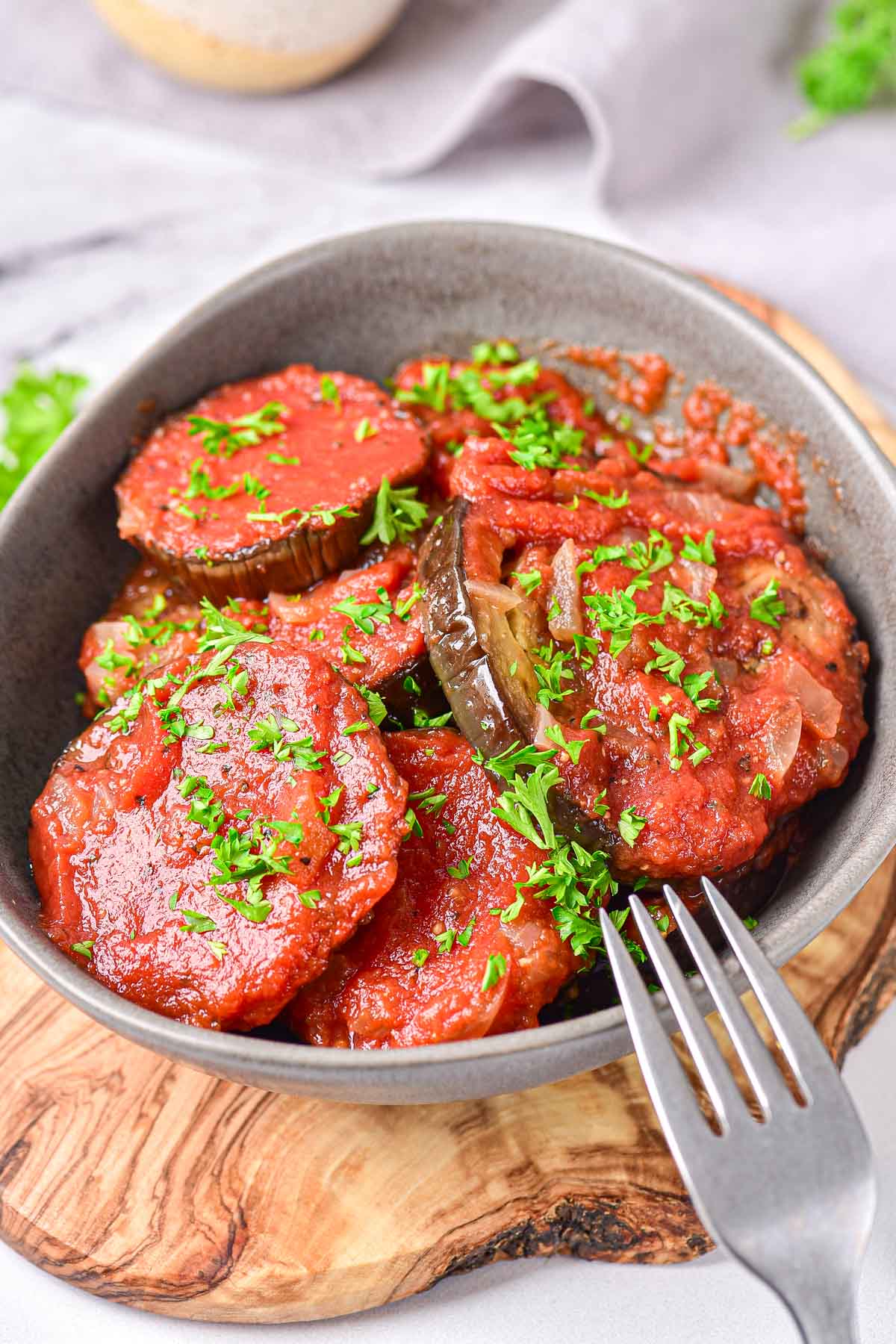 fried eggplant covered in red tomato puree in grey bowl with fork beside.