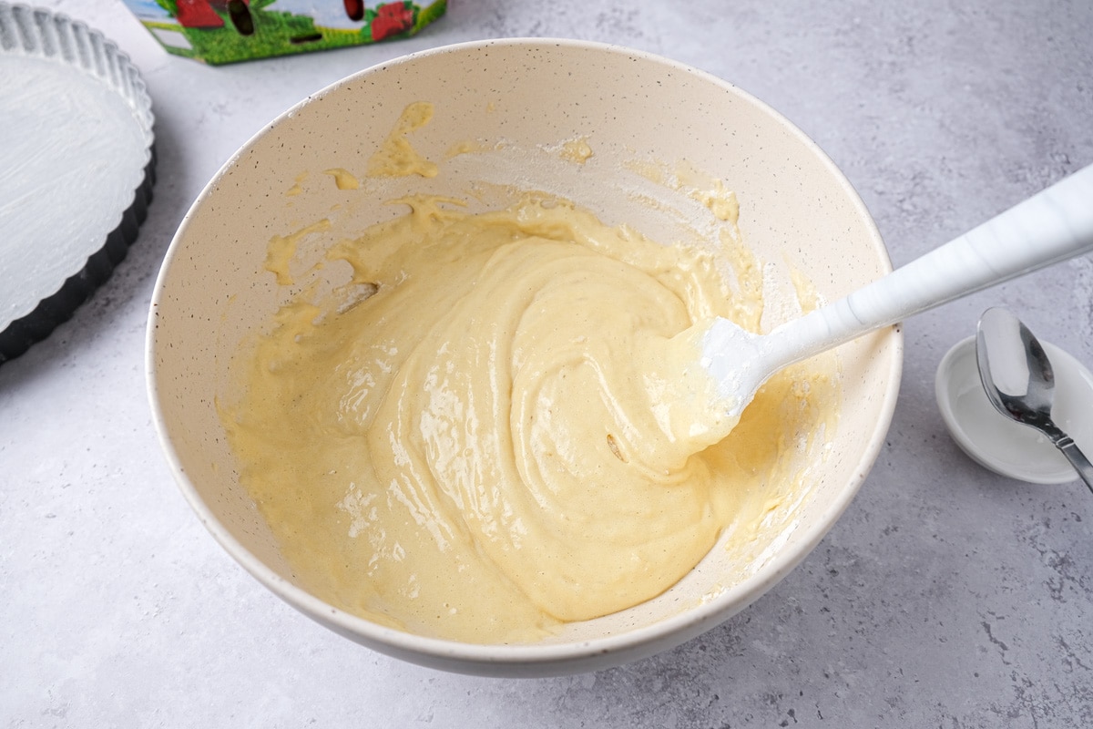 white spatula folding cake batter into large mixing bowl on counter.