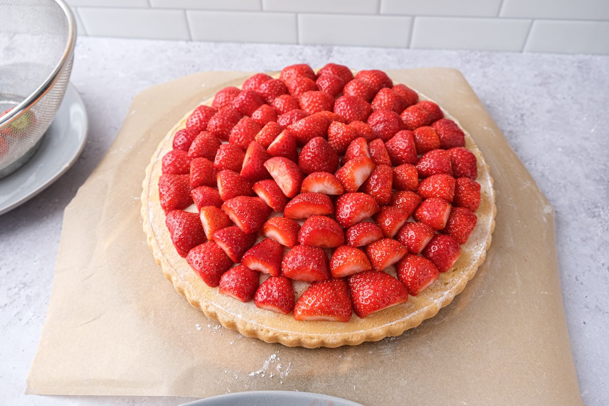 flat cake bottom covered in strawberries placed in rings sitting on parchment paper.