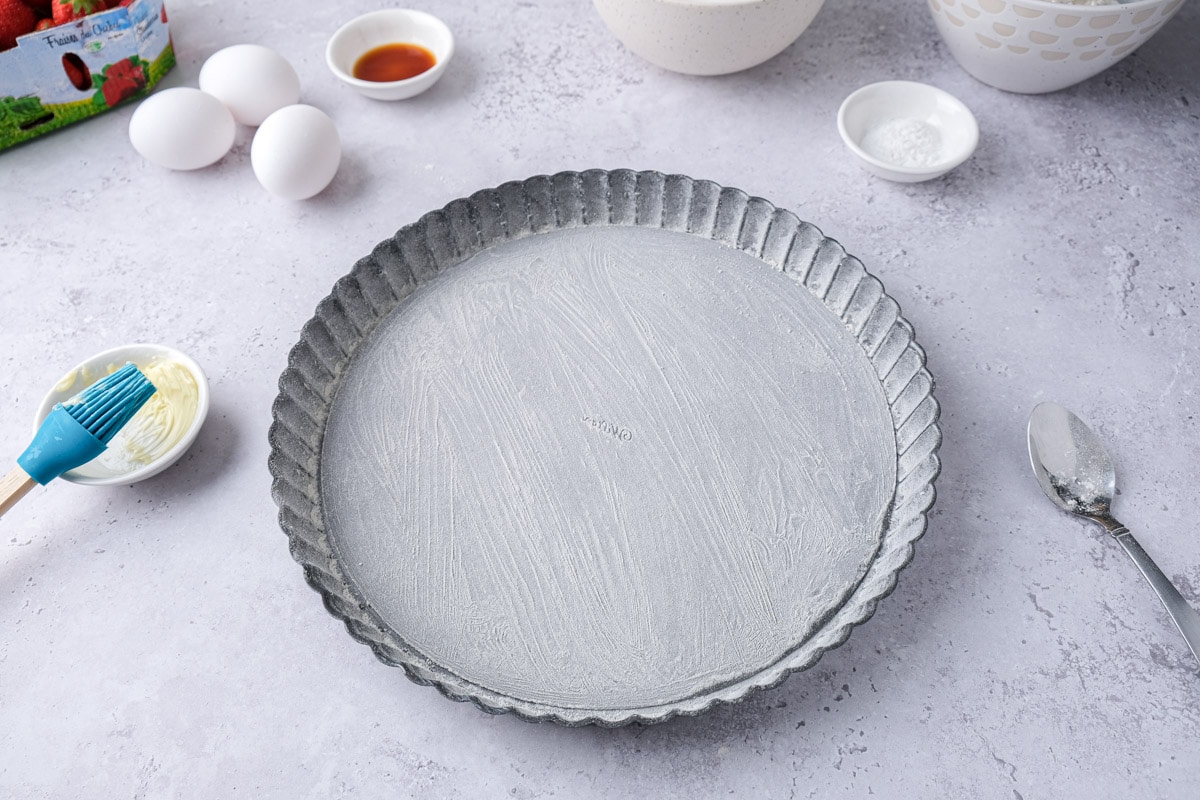 round silver cake pan coated in butter on counter top.