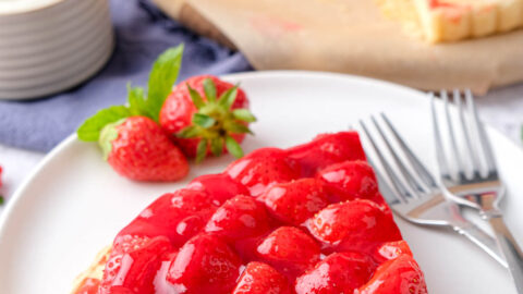 slice of red strawberry cake on plates with forks and berries beside.