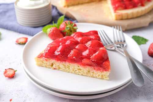 triangle slice of strawberry cake on white plate with forks beside.
