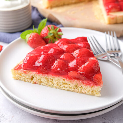 triangle slice of strawberry cake on white plate with forks beside.