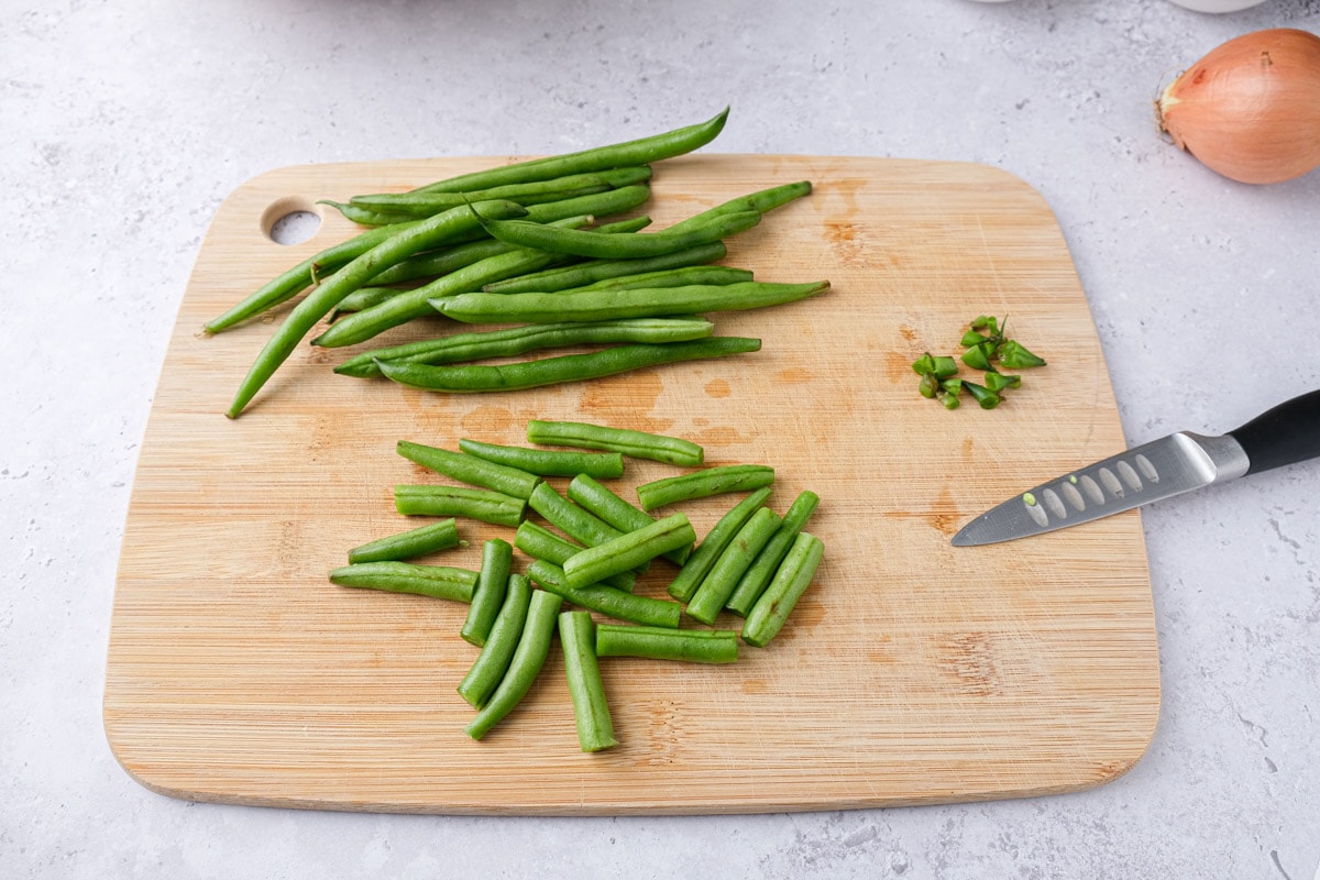 green beans being trimmed on wooden cutting board with knife beside.