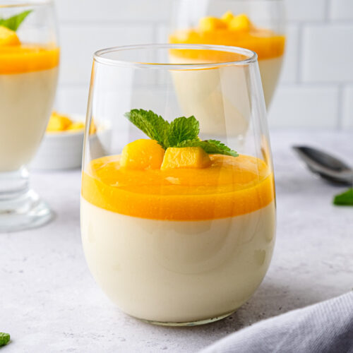 glass of mango panna cotta with mint leaves on top on counter.