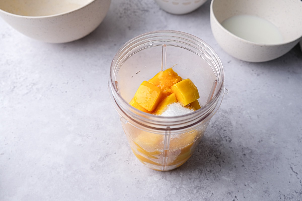 mango chunks and sugar in plastic tumbler for mixing.