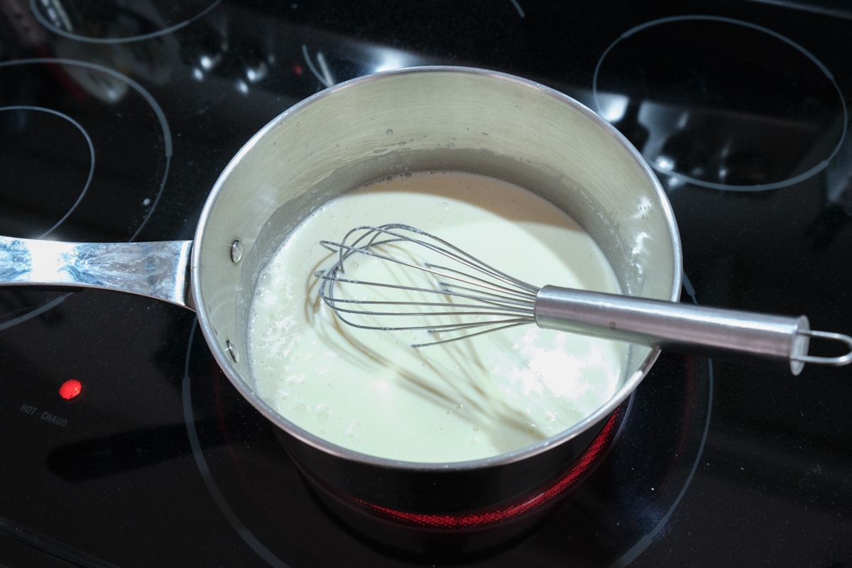 silver whisk mixing cream in silver pan on black stove top.