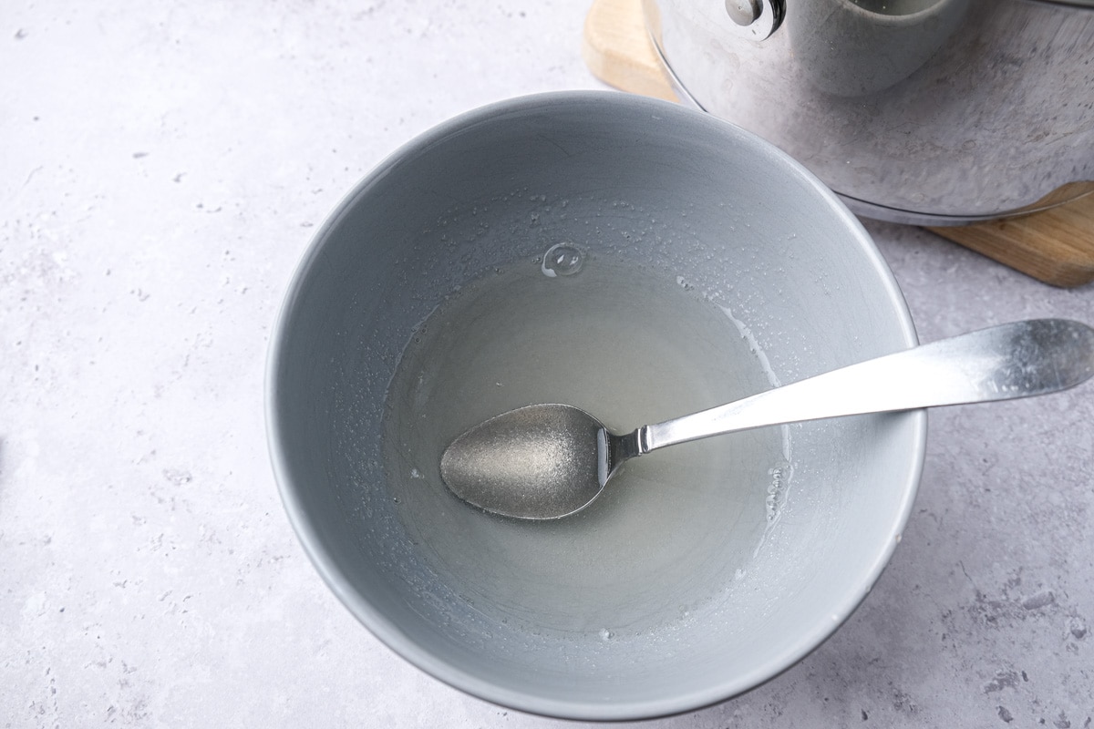 gelatin powder in water mixed with silver spoon in blue bowl.