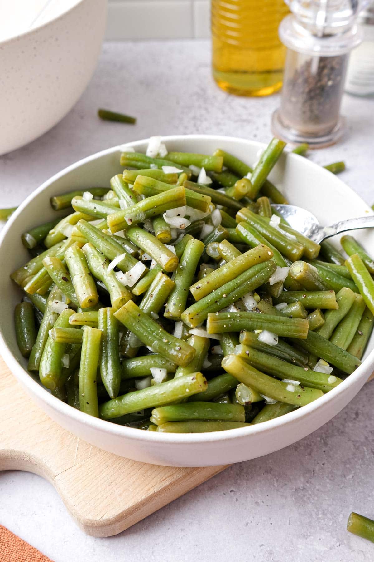 bowl of green bean salad with onion on wooden board on counter.