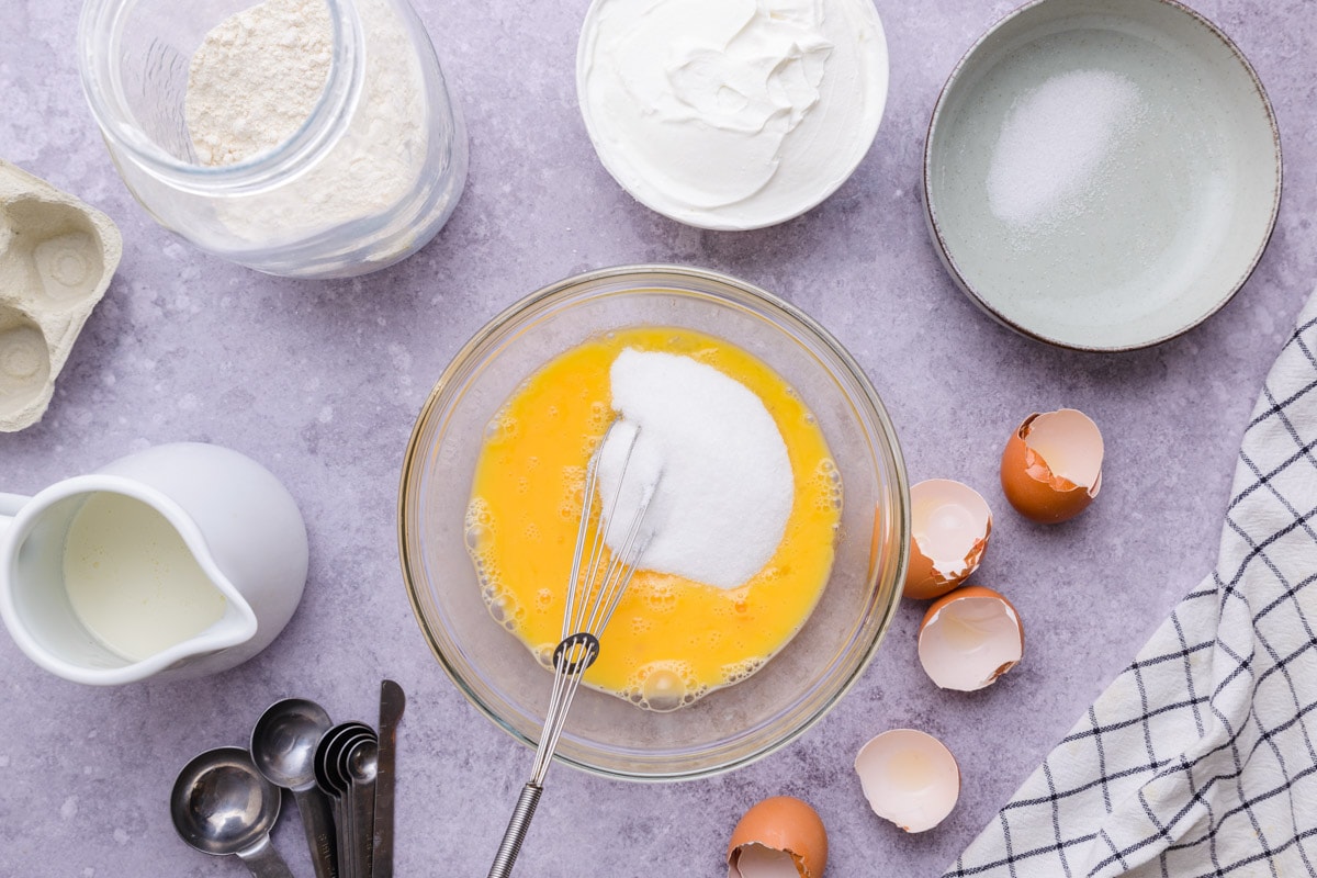 silver whisk mixing cream cheese into egg yolks in mixing bowl.