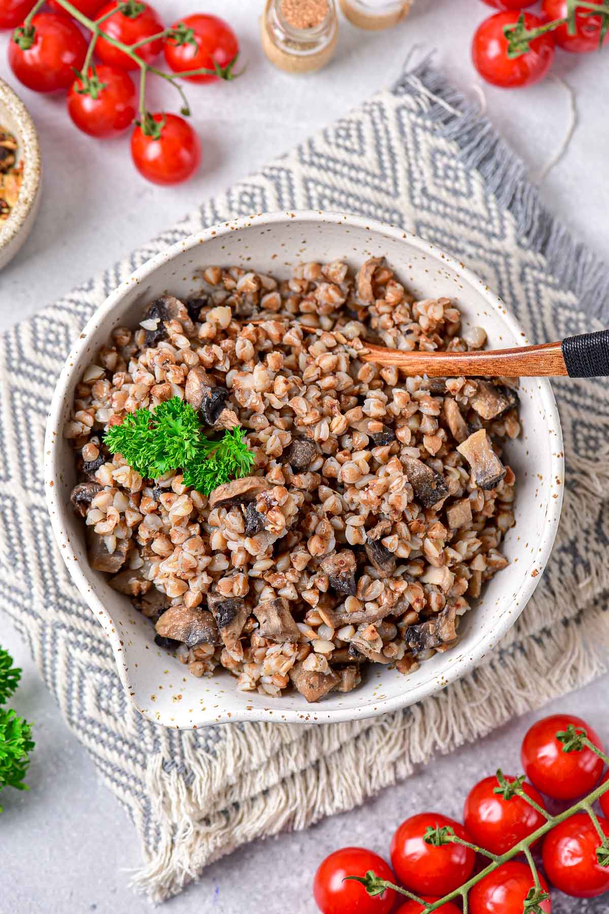 white bowl of buckwheat porridge with mushrooms with wooden spoon sticking out.