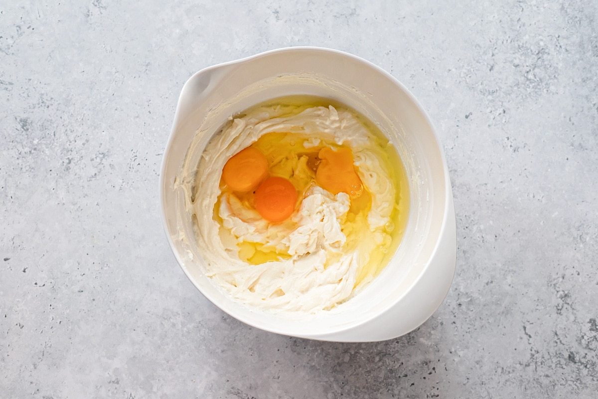 raw eggs in white mixing bowl full of ricotta cheese sitting on counter.