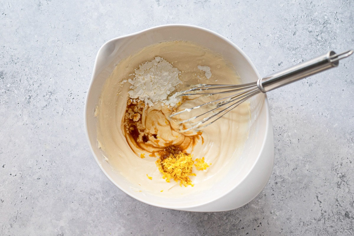 vanilla extract mixed into cheesy blend in white mixing bowl on counter.