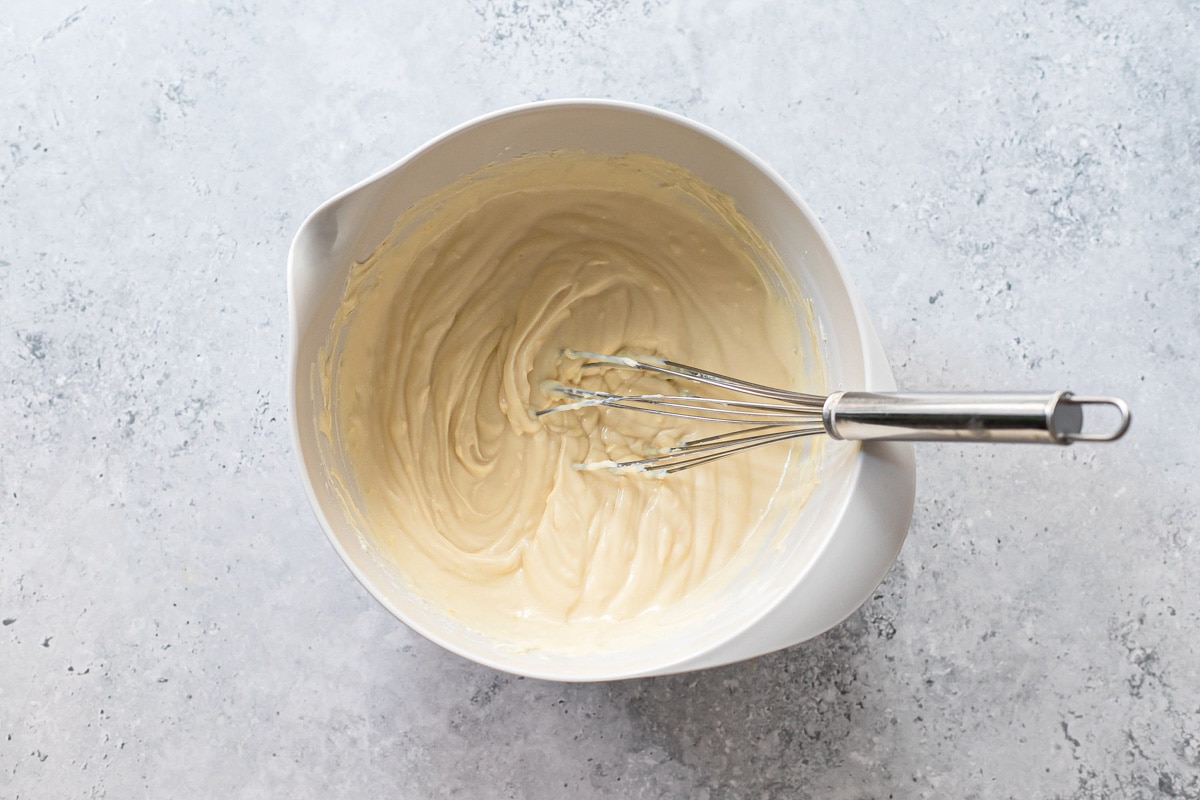 creamy cheese blend in white mixing bowl with silver whisk sticking out.