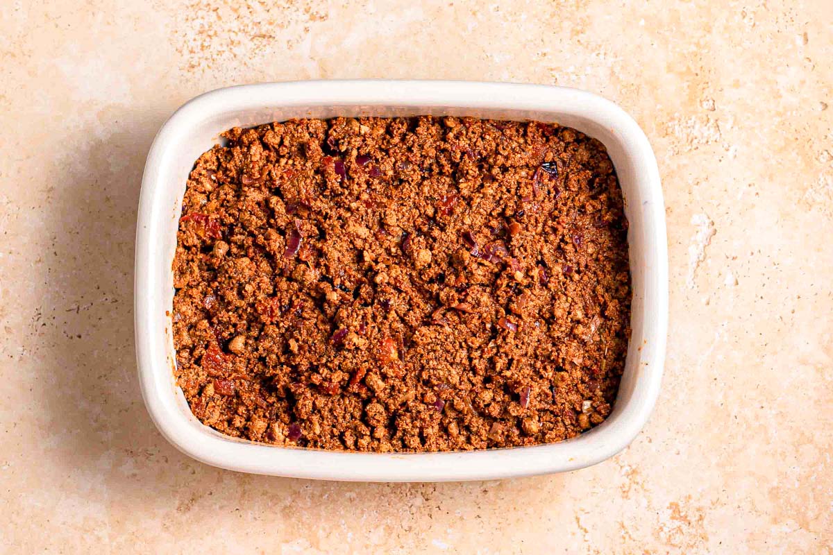 layer of tomato sauce and ground meat in white baking dish on counter.