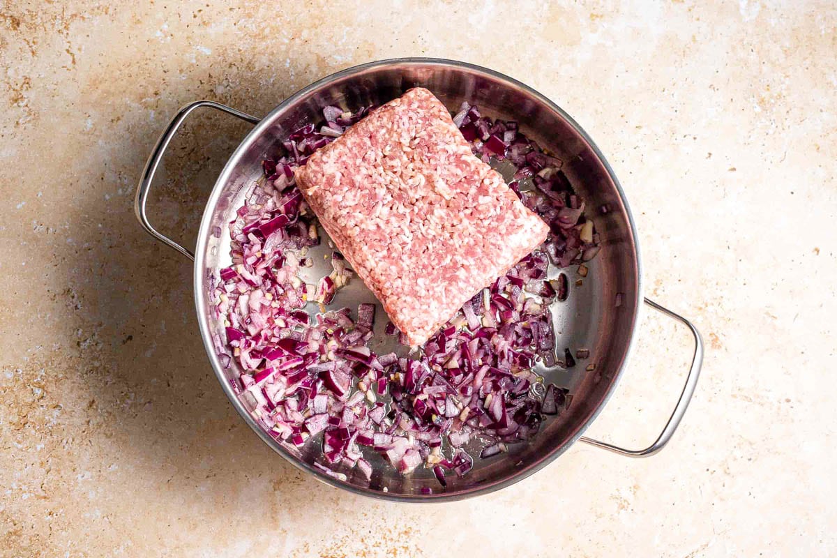 rectangle of ground beef in silver pot with bed of fried onions inside.
