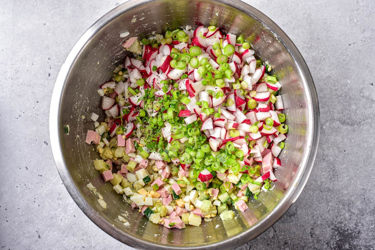 chopped green onion and radishes on top of other vegetable ingredients in silver bowl.