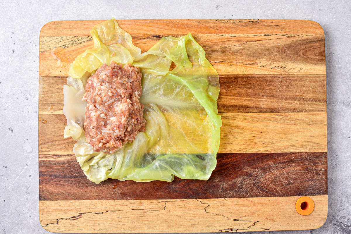 rice and meat filling sitting at edge of cabbage leaf on wooden cutting board.