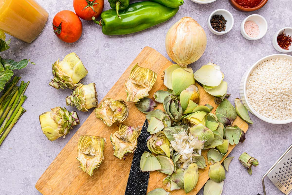 fresh artichokes on wooden cutting board with other ingredients around.