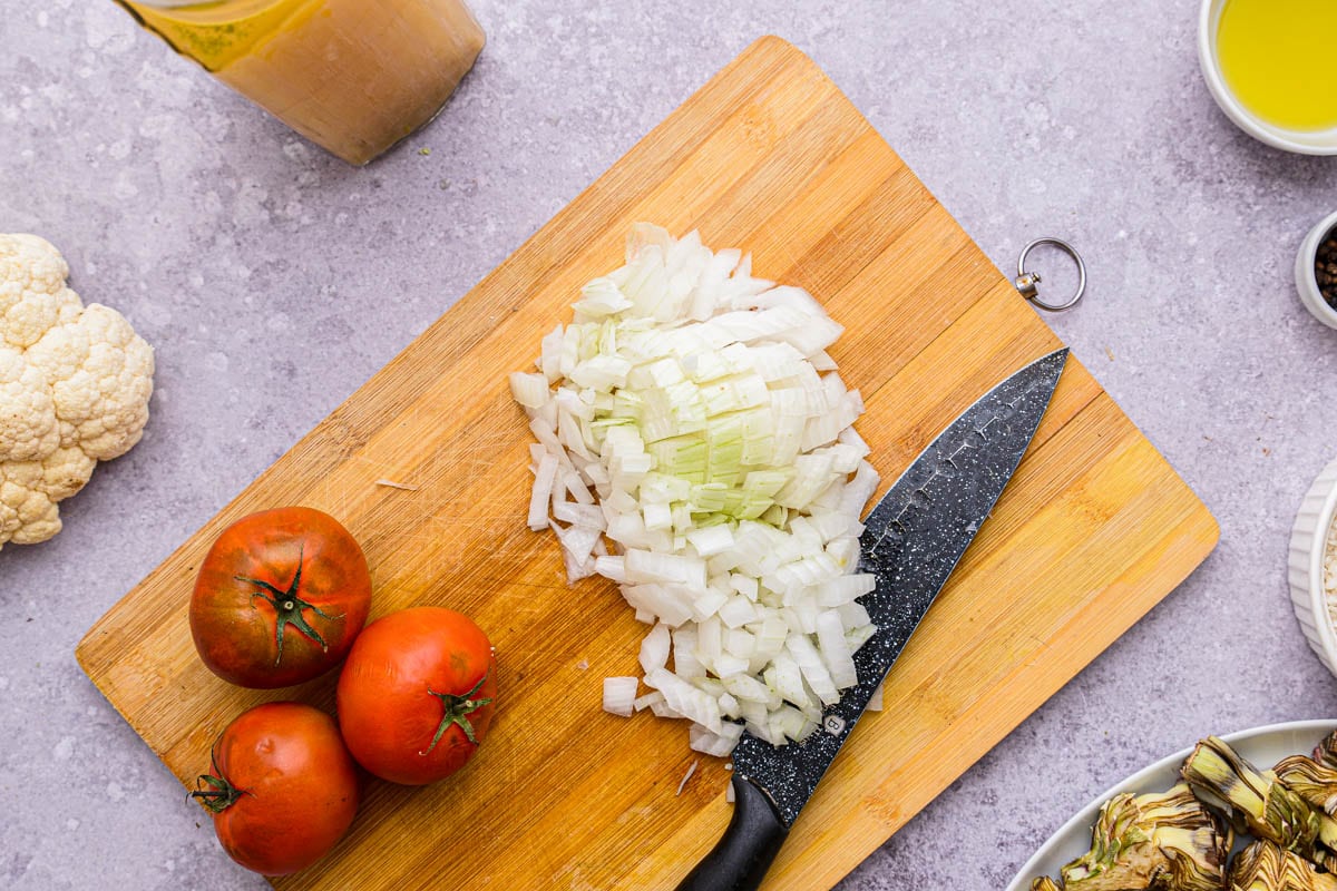 diced onion on wooden cutting board beside whole tomatoes.