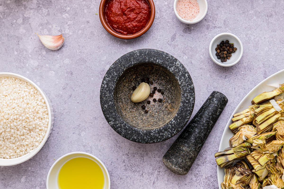 black mortar with black pepper and garlic clove inside beside pestle on counter.