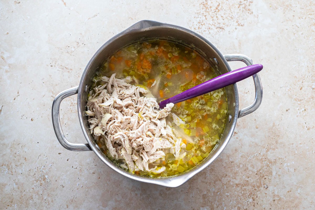 large pot of lemon chicken soup with purple spoon sticking out of it.