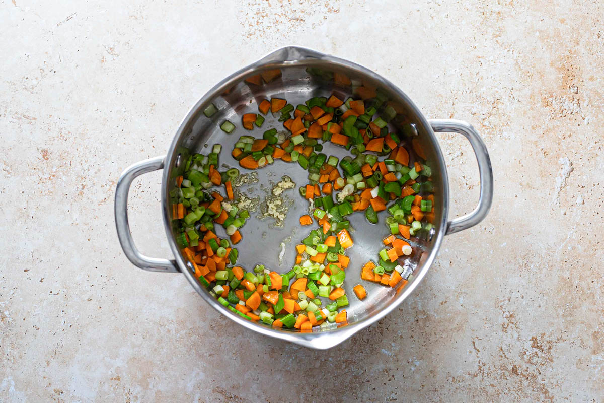 chopped vegetables frying in bottom of tall silver pot.
