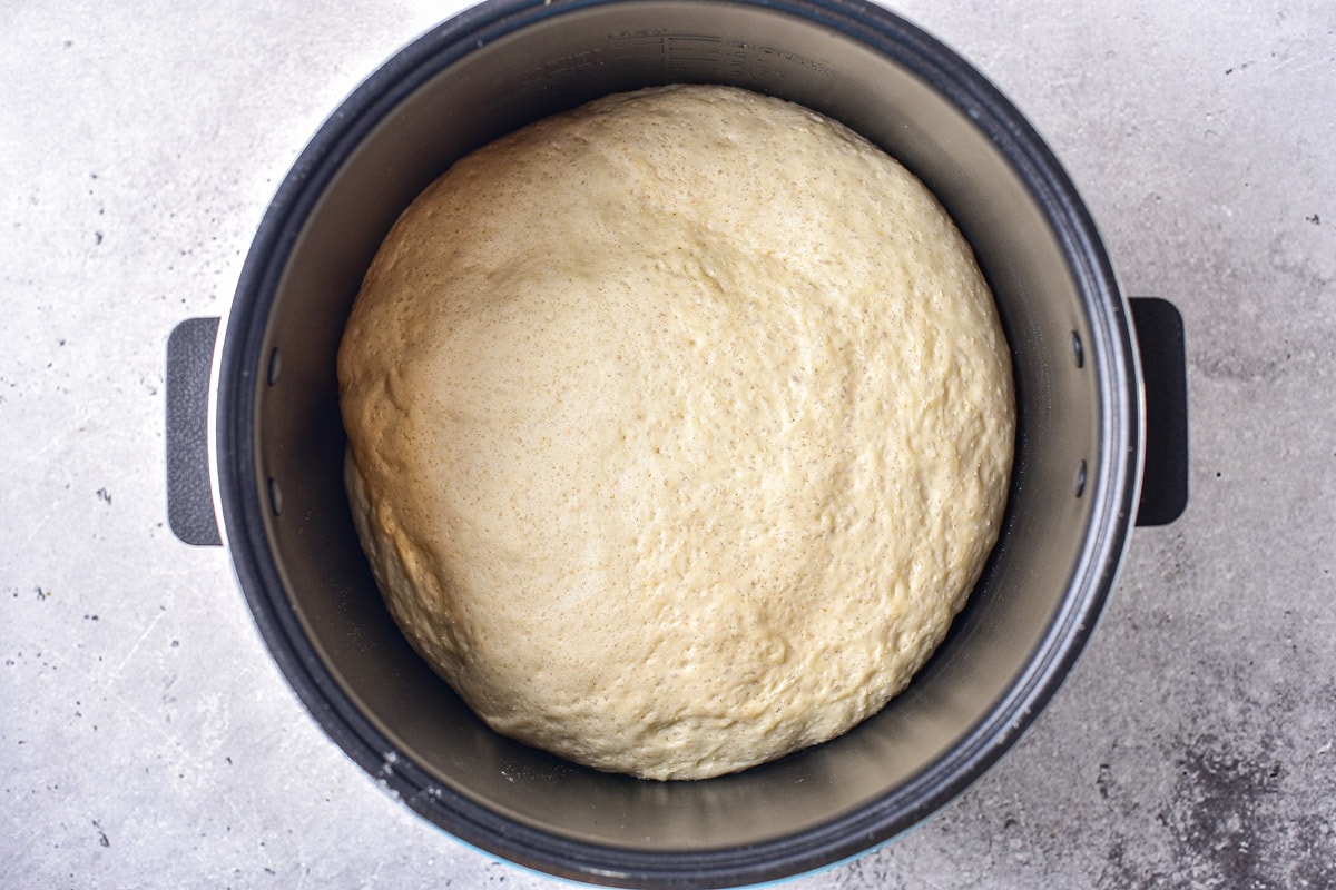 risen ball of yeast dough in silver pot on counter top.