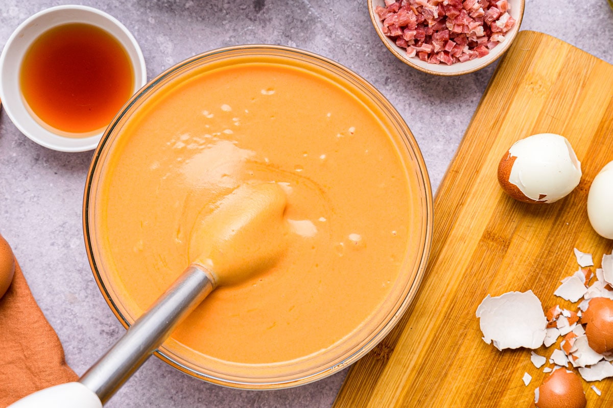 creamy tomato soup in large glass bowl on counter with immersion blender in the broth.