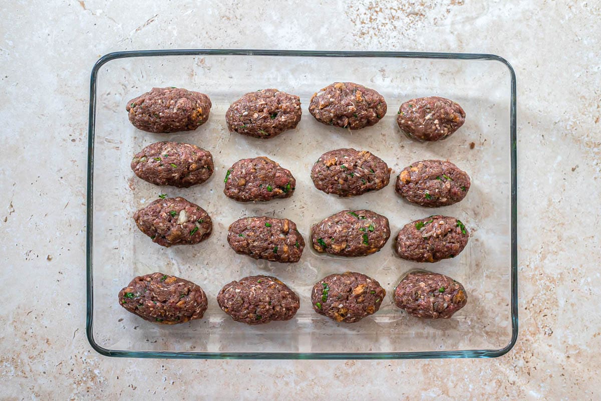 sixteen oval shaped meatballs in glass baking dish on counter.