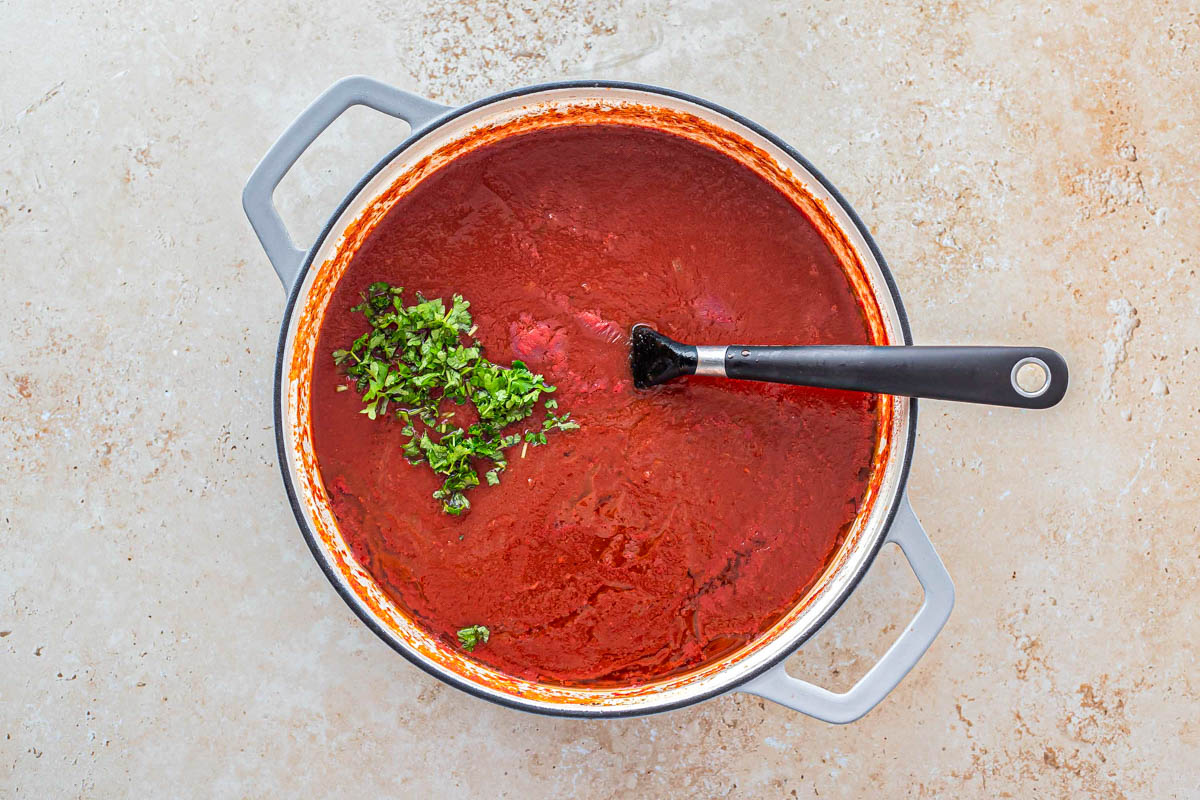 tomato sauce in large pot with chopped parsley on and mixing spoon in the sauce.