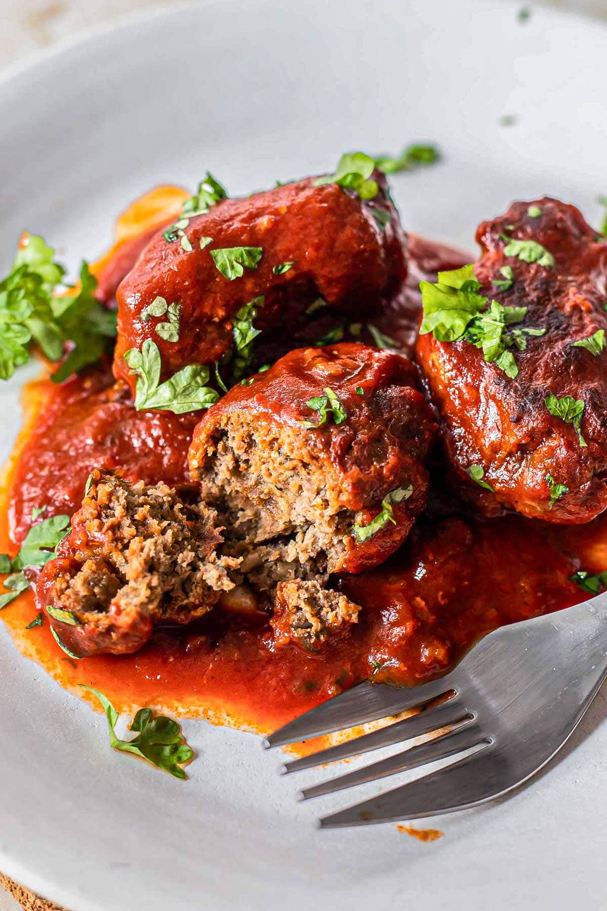 meatballs in tomato sauce on plate with fork cutting one in half.