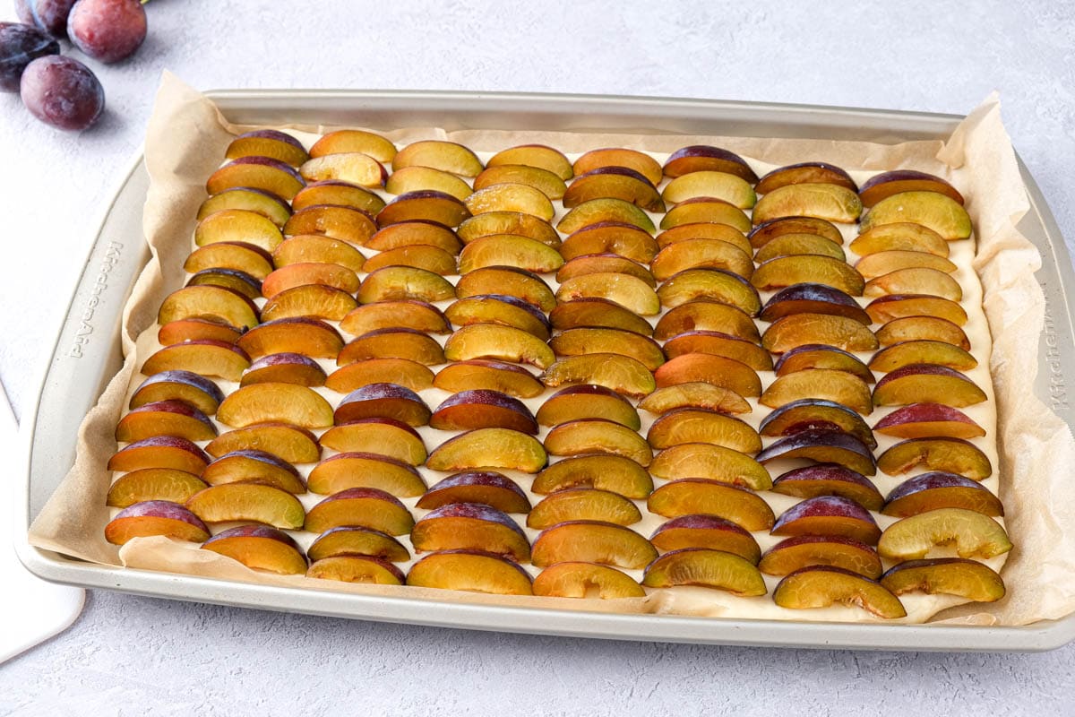 sliced plums covering sheet pan of cake sitting on counter.
